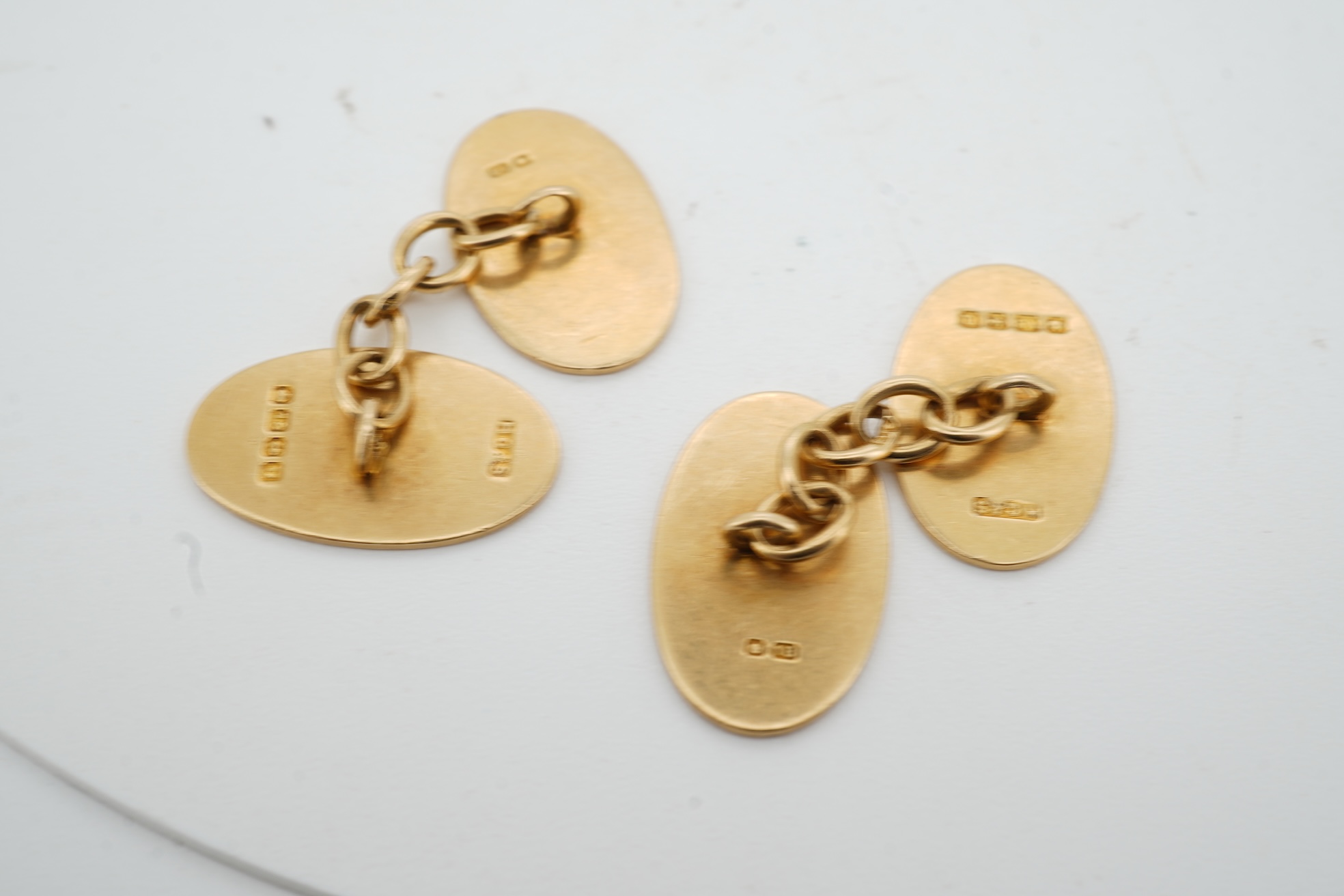 A pair of 18ct gold cufflinks, each end of oval outline, connected by chain linking, engraved with the initials RWA, length 1.8cm each, British hallmarks, combined gross weight approximately 7.5 grams